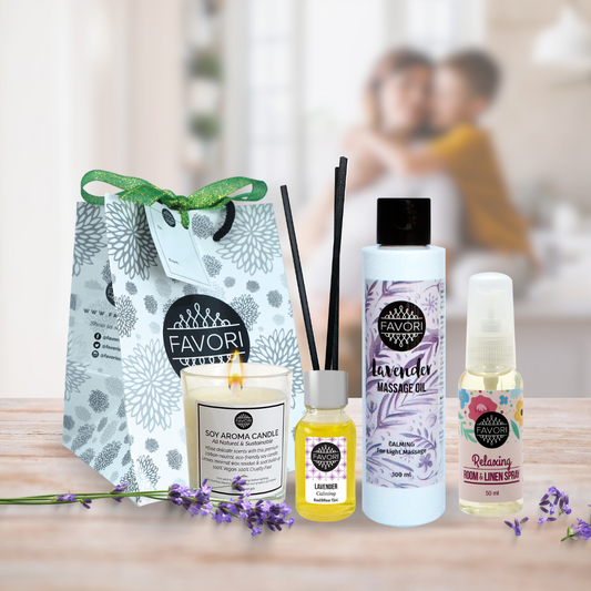 A gift set on a wooden table, including a MOTHER’S DAY Lavender Relaxation Gift Package from FAVORI Scents, which includes a lavender massage oil bottle, a soy candle, two small spray bottles, and reed diffusers, all displayed beside a bag. In the blurry background