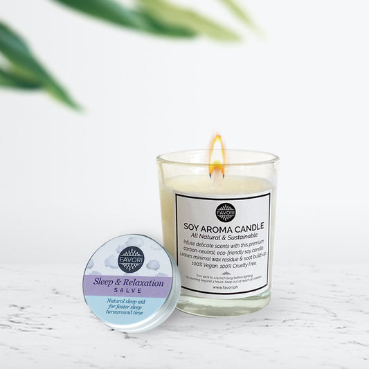 A 15g tin of FAVORI Scents Wellness Salve and a 60g FAVORI Scents Soy Aroma Candle on a white surface with a blurred plant in the background.