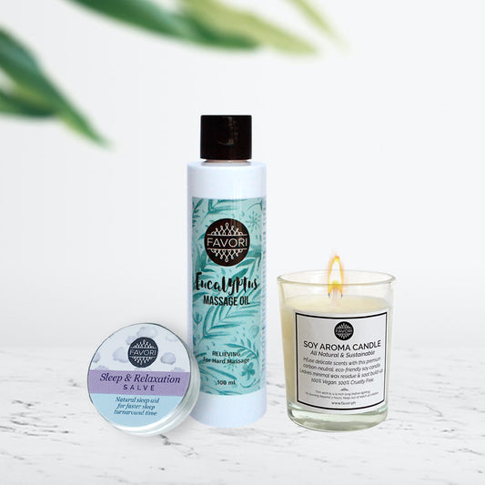 A set of FAVORI Scents wellness products on a counter, including a tin of Wellness Salve (15g), a bottle of eucalyptus Massage Oil (100ml), and a lit Soy Aroma Candle (60g).