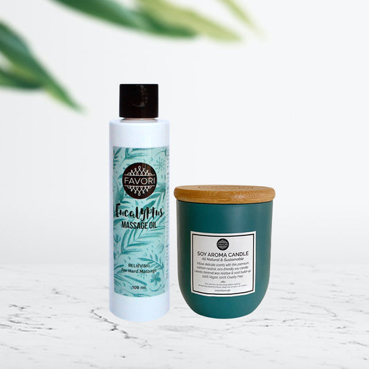 Sentence with replaced product names: A FAVORI Scents massage oil bottle and a FAVORI Scents soy aroma candle in a gift package on a countertop with a plant shadow in the background.