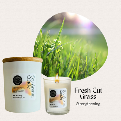 FAVORI Scents All Occasion white soy candle with wooden lid, beside a lit candle on sunlit green grass.