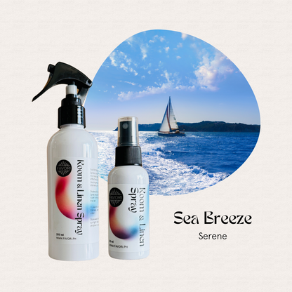 Two FAVORI Scents Regular Room & Linen Air Sprays sit before a sailboat on blue water under a cloudy sky.