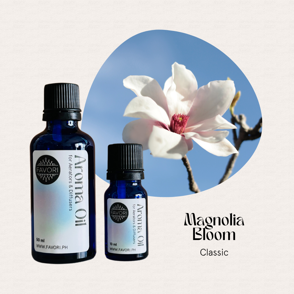 Two FAVORI Scents Aerator/Diffuser Aroma Oils placed beside a blooming magnolia under a clear blue sky.