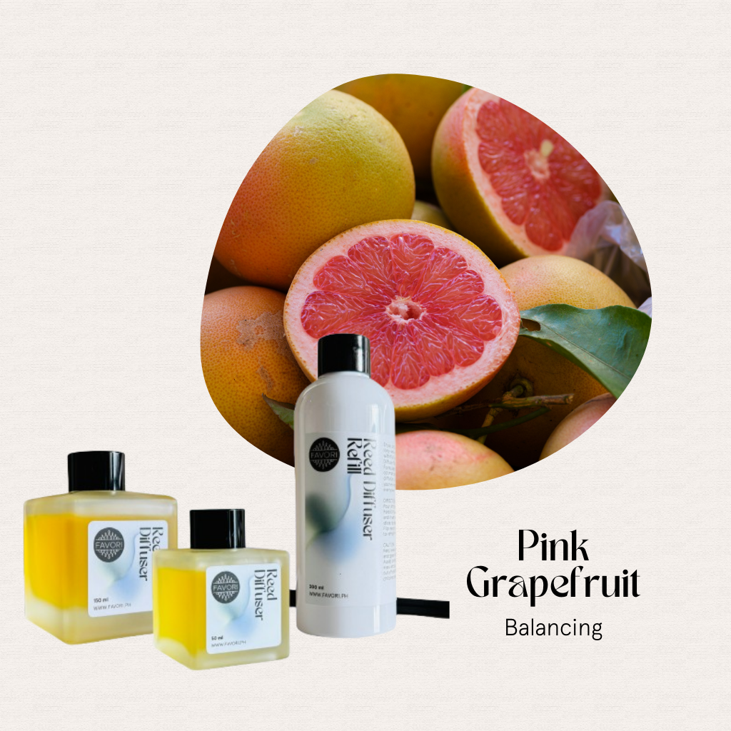 A halved pink grapefruit sits with whole ones and three FAVORI Scents Pink Grapefruit Trio Reed Diffusers.
