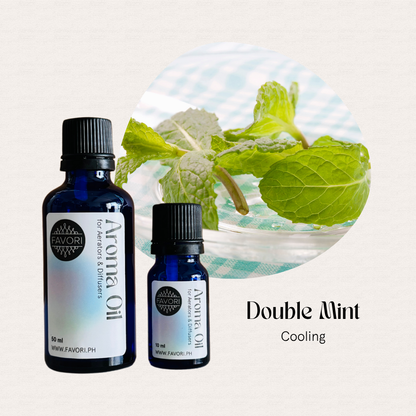 Two blue bottles of FAVORI Scents AD Aroma Oils next to fresh mint leaves in a clear bowl.