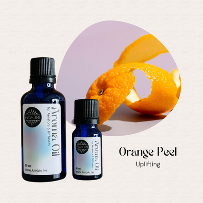 Two blue FAVORI Scents AD Aroma Oils labeled Orange Peel beside a fresh orange peel on a light background.