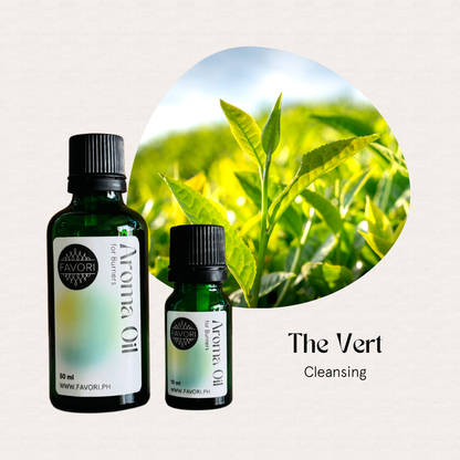 Two green bottles of FAVORI Scents Burner Aroma Oils labeled The Vert beside fresh green tea leaves.