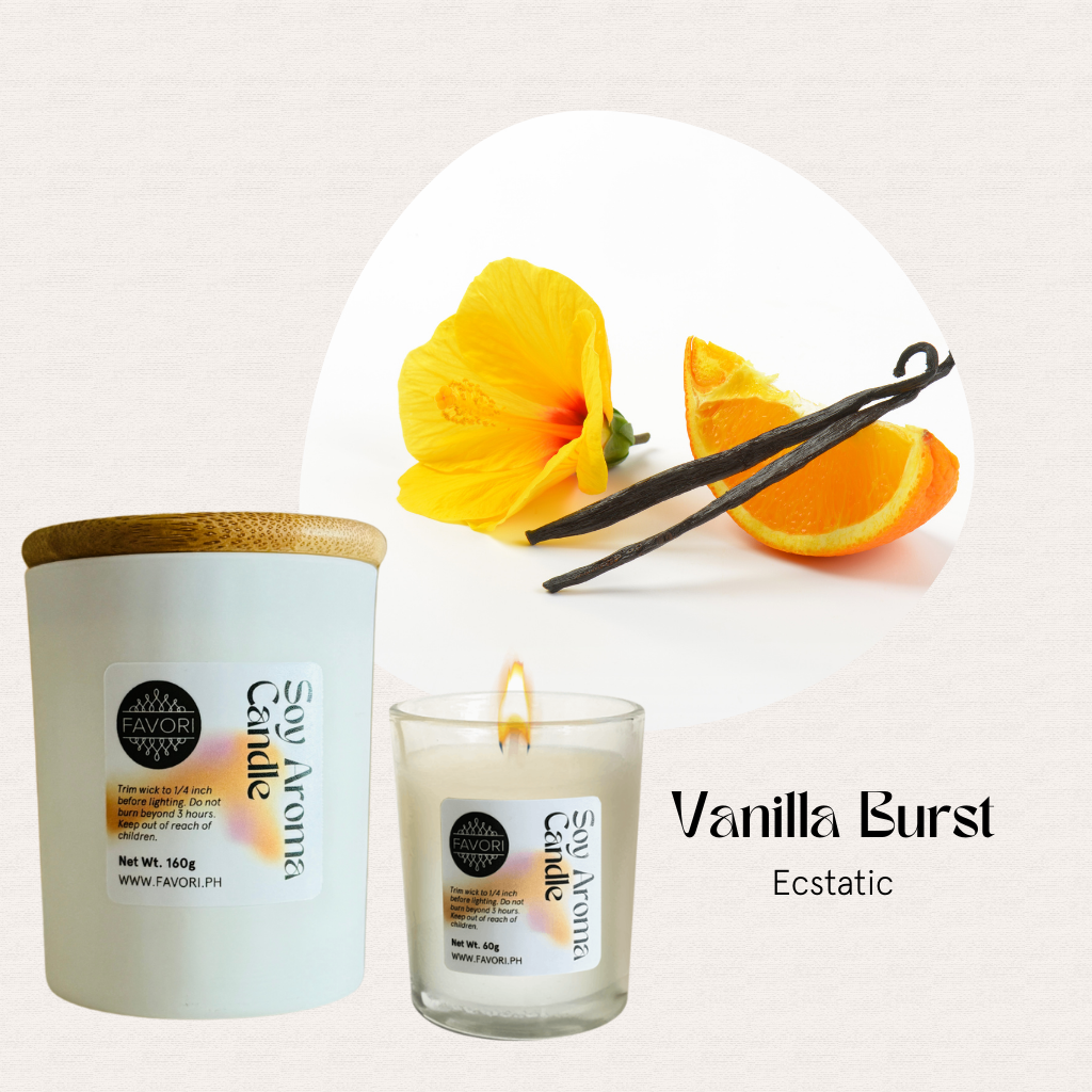 FAVORI Scents All Occasion soy candle, lit, with hibiscus flower, orange slice, and vanilla pods.