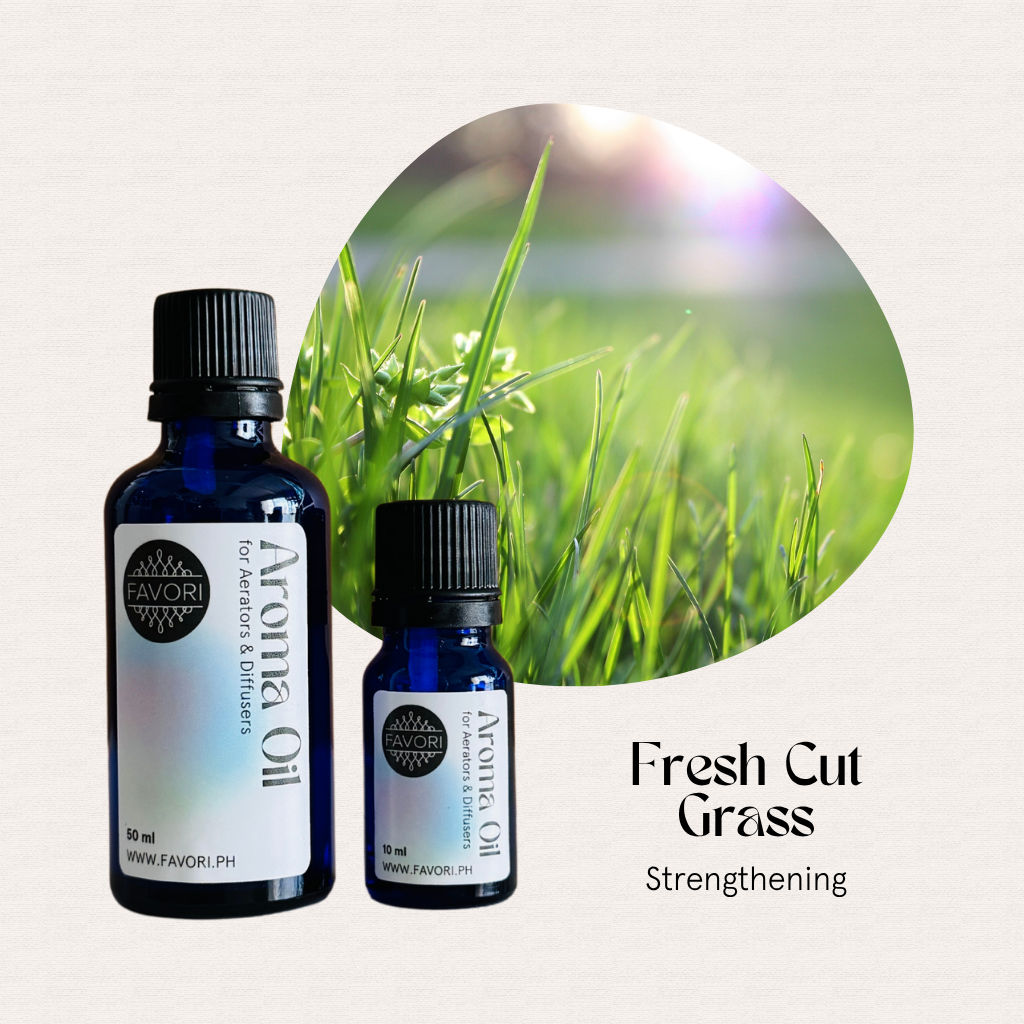 Two blue bottles of FAVORI Scents AD Aroma Oils, Fresh Cut Grass, sit beside fresh green grass.