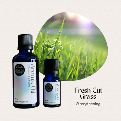 Two blue bottles of FAVORI Scents AD Aroma Oils, Fresh Cut Grass, sit beside fresh green grass.