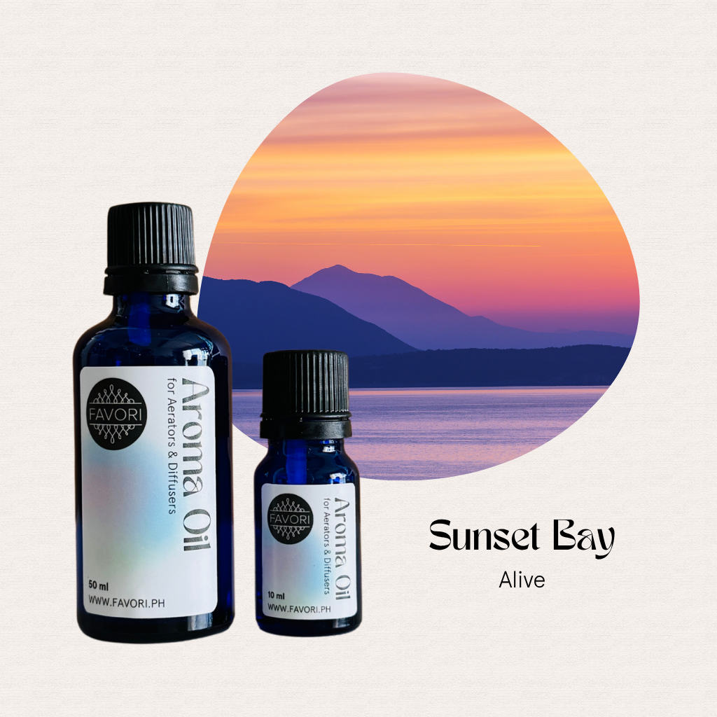 Two blue bottles of FAVORI Scents AD Aroma Oils set before a sunset bay, mountains, and calm water.