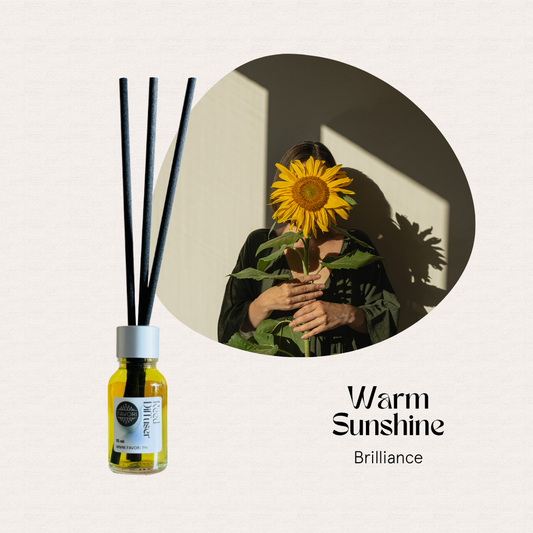 A woman holds a sunflower near her face beside a FAVORI Scents Warm Sunshine Mini Reed Diffuser (MRD).