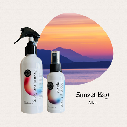 Two FAVORI Scents Regular Room & Linen Air Sprays in front of a vivid sunset, text: Sunset Bay Alive.