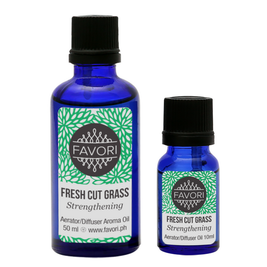 Two bottles of Fresh Cut Grass Aerator/Diffuser (AD) Aroma Oil by FAVORI Scents. The larger is 50 ml and the smaller is 10 ml. Both come in blue glass bottles with black caps and labels featuring a green leafy design and the FAVORI logo. Ideal for use with diffuser devices, the text reads "Strengthening.