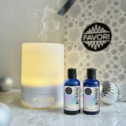 A lit FAVORI Scents Lind Diffuser mists beside two 50ml Aroma Oils and a Favori gift package.