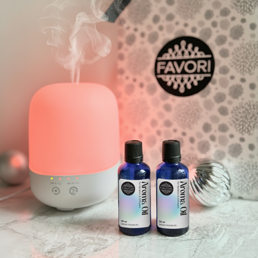 A lit FAVORI Scents Capsule Diffuser with two 50ml aroma oils beside a patterned gift box.