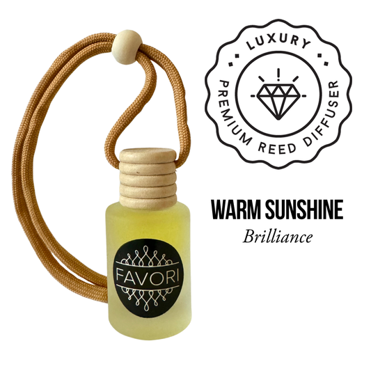 A small glass bottle labeled "FAVORI Scents," filled with yellow liquid and topped with a wooden cap, serves as a compact diffuser. A tan braided cord loops through the cap with a wooden bead. Beside it, a circular seal with a diamond icon and text reads "Luxury Premium Reed Diffuser." Below, the text states "Warm Sunshine Hanging Aroma Diffuser (HAD) Brilliance.