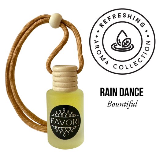 A small, translucent bottle of "FAVORI Scents" essential oil, featuring a wooden cap and a tan cord looped through it. The label reads "FAVORI Scents". Above the bottle, a circular badge states "Refreshing Aroma Collection" with an icon of a droplet and leaf. Text beside it reads "Rain Dance Hanging Aroma Diffuser (HAD)". This compact and portable fragrance promises a long-lasting aroma perfect