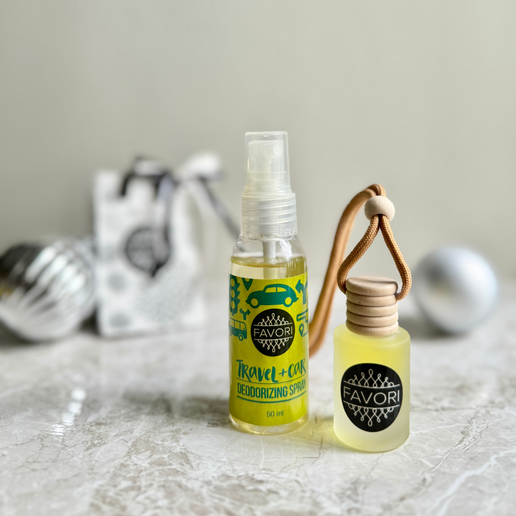 Displayed are two FAVORI Scents deodorizing products: a 50ml Air Spray with a green travel-themed design labeled "Travel + Car," and a small Hanging Aroma Diffuser featuring a wooden cap and cotton cord. These products are set against a neutral background, complemented by blurred decorative silver ornaments.