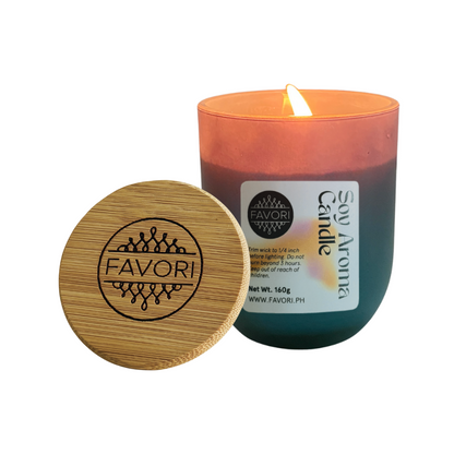 A lit Yuletide Occasion soy candle by FAVORI Scents in a blue glass jar beside an engraved wooden lid.