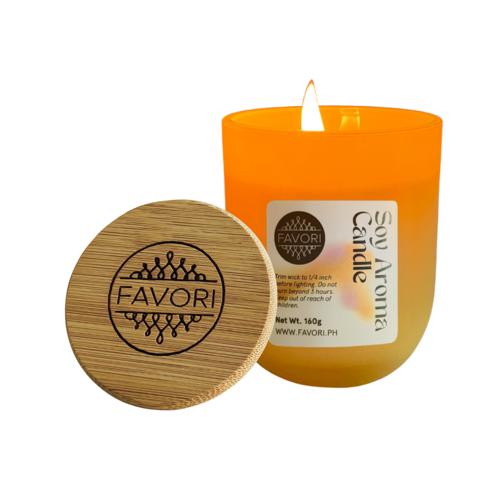 A lit Yuletide Occasion soy candle by FAVORI Scents, orange with engraved lid and clear label.