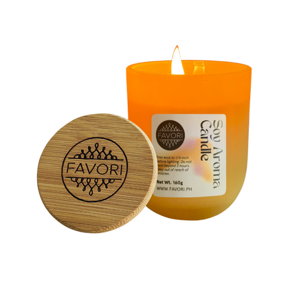 A lit Yuletide Occasion soy candle by FAVORI Scents, orange with engraved lid and clear label.